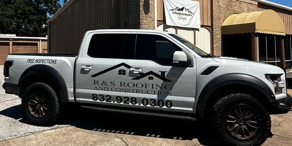 White pickup truck with R&S Roofing and Construction branding parked outside a building.