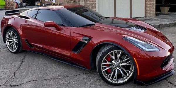 Glossy maroon sports car parked outside a building with a sign.