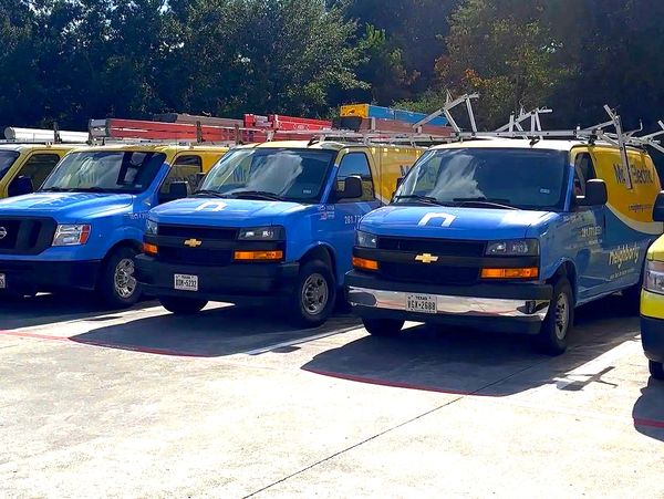 Blue and yellow service vans parked in a lot with ladders on top.