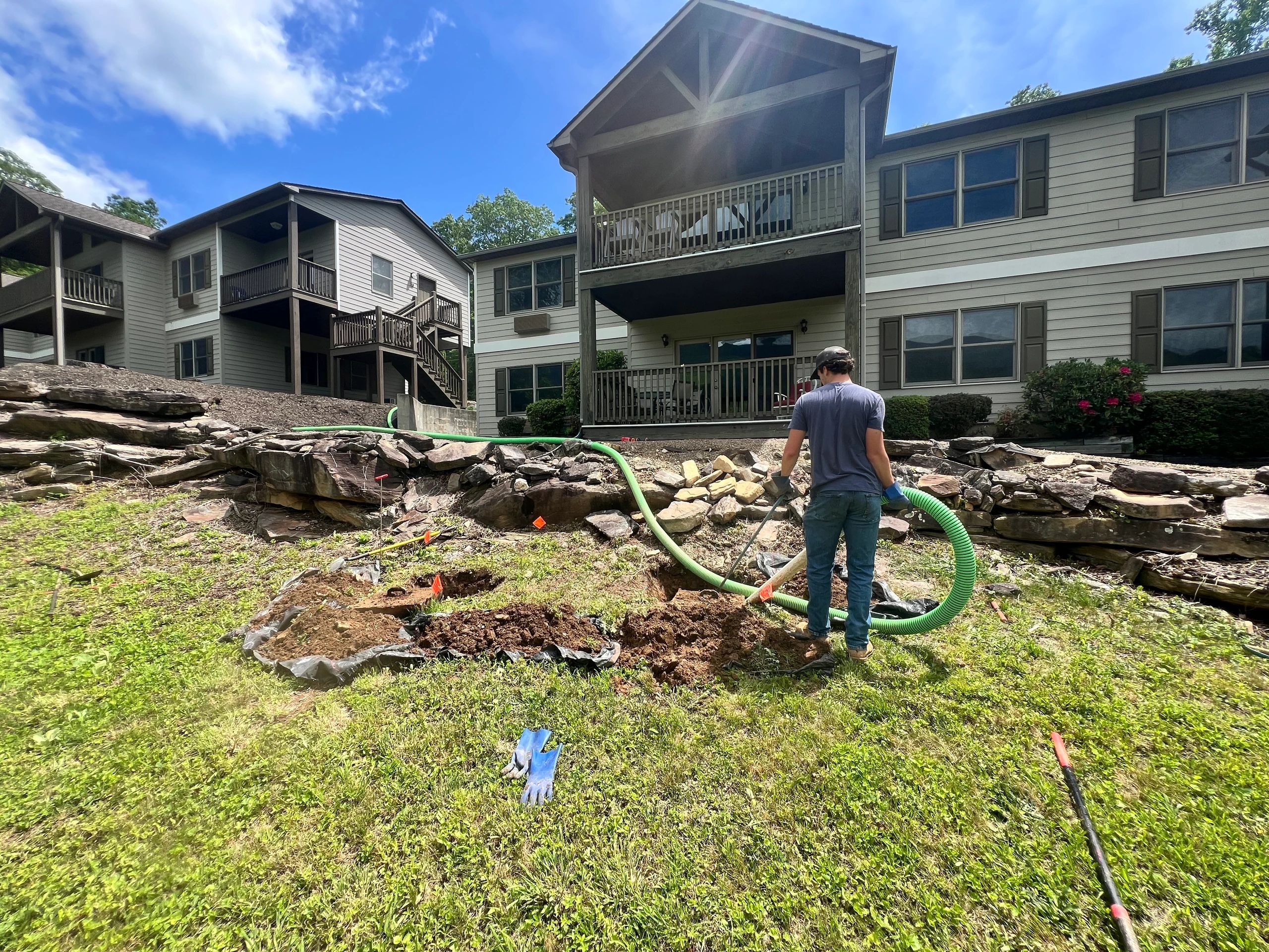 Man working outside a two-story house with a large green hose.