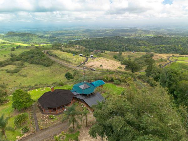 Scenic aerial view of a countryside house surrounded by lush green hills and winding roads.