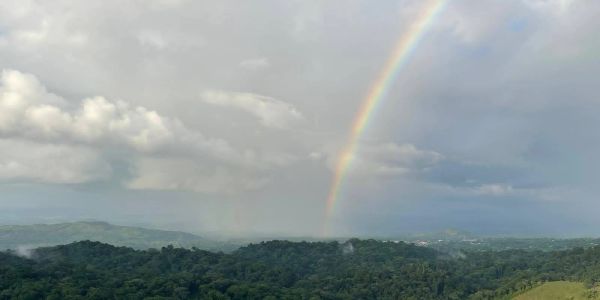 Rainbow over lush green hills and cloudy sky.