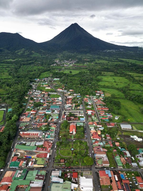 Aerial view of a town with a volcano in the background under cloudy skies.