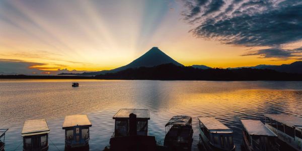 Sunset over a lake with boats and a mountain silhouette.