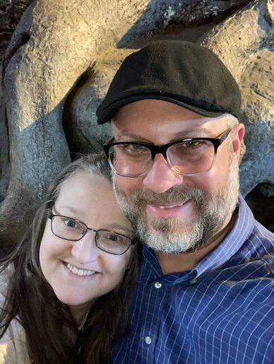 Smiling couple wearing glasses and posing closely together.