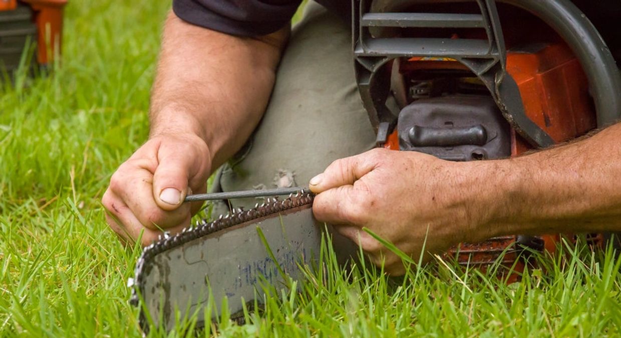 A person sharpening a chainsaw blade on grass.