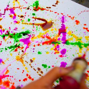 Colorful paint splatters creating abstract art on white paper.