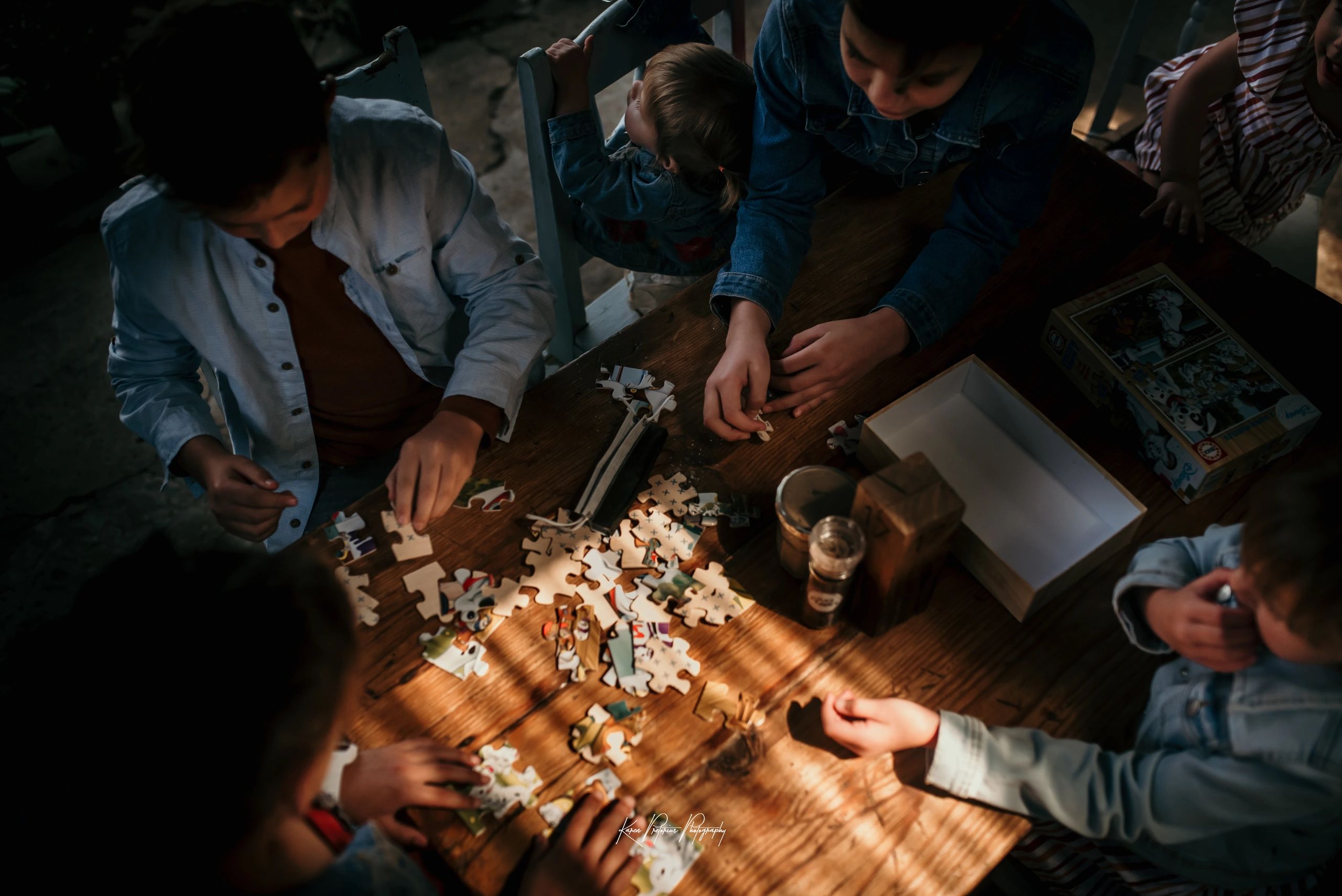 Children assembling a puzzle at a wooden table.