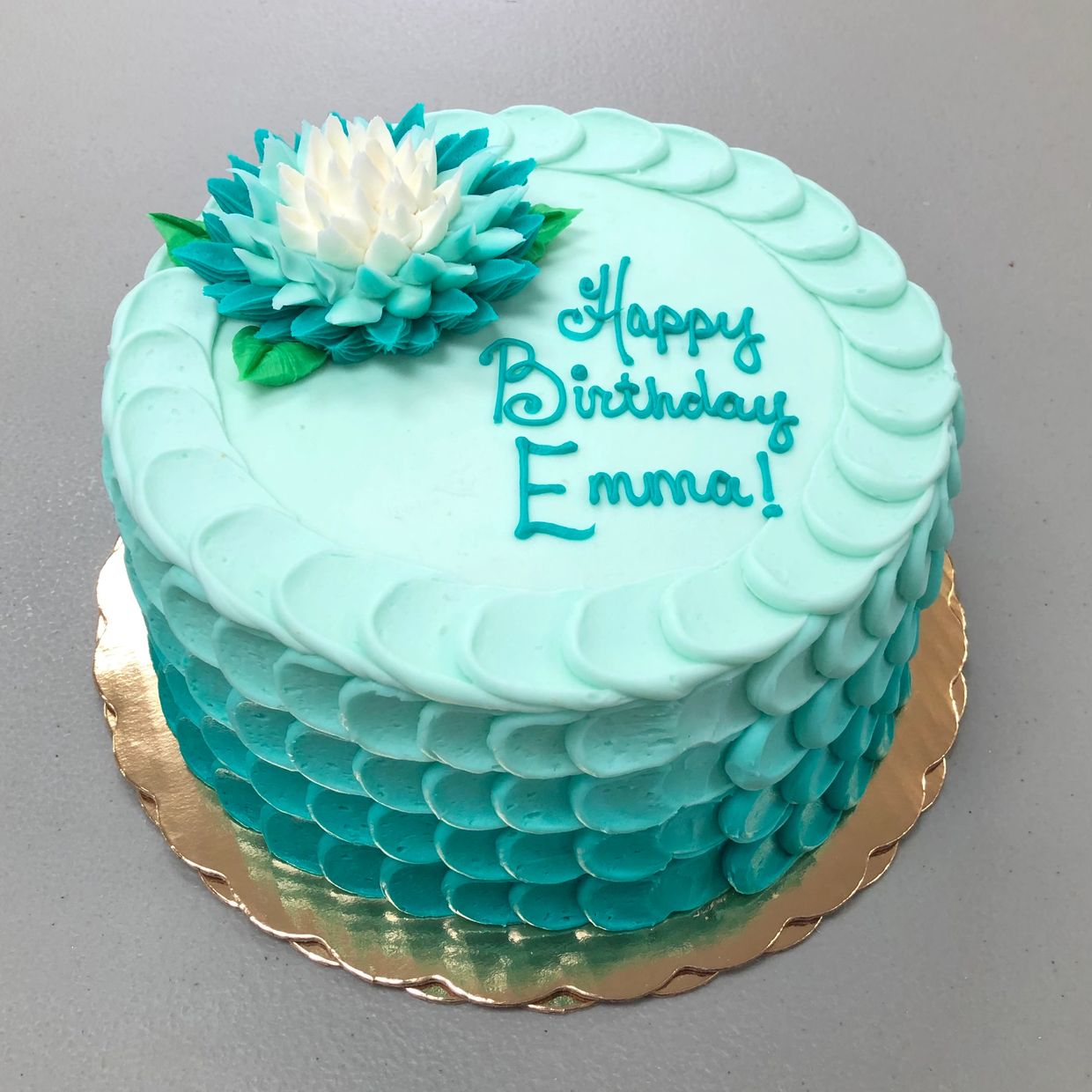A blue colored birthday cake to Emma with flower