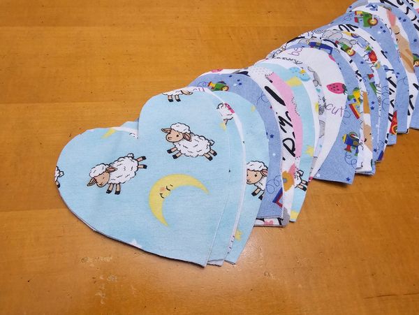 Heart-shaped fabric pieces with various cute patterns on a wooden surface.