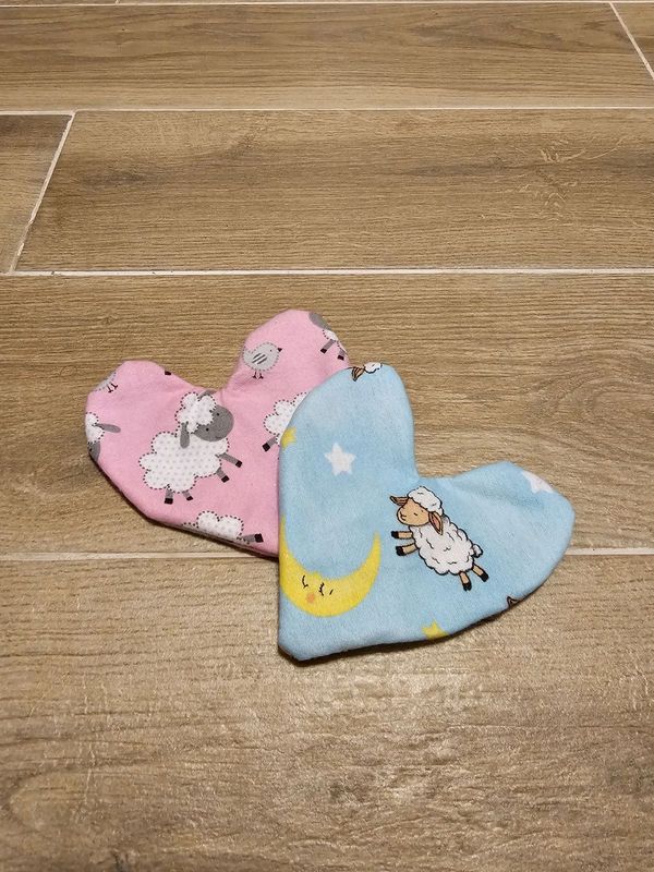 Two heart-shaped fabric pieces with sheep patterns on wooden floor.
