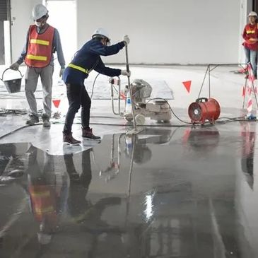 Workers polishing a concrete floor inside a building under construction.