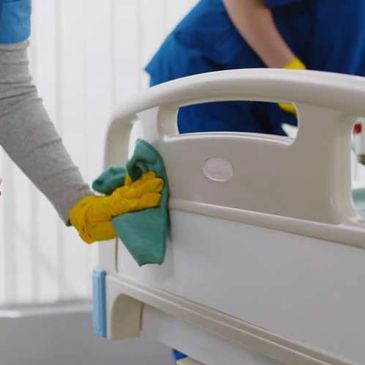 Person cleaning hospital bed rail with gloves and cloth.