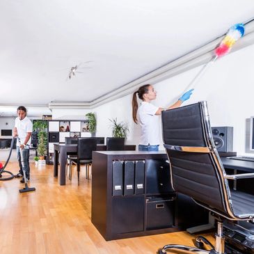 Two people cleaning a modern office with vacuum and duster.