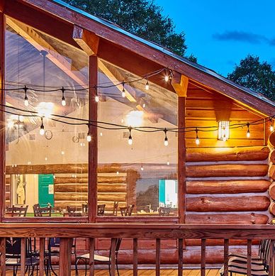 Cozy log cabin with string lights and large glass windows at dusk.