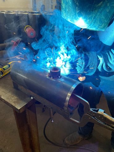 A person welding metal with bright blue sparks and smoke.