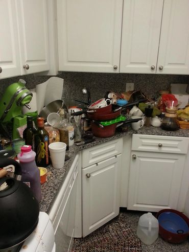 Cluttered kitchen counter with various utensils, bottles, and dishes piled up.