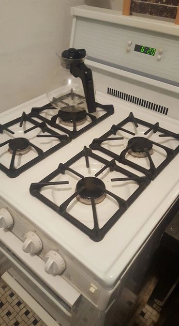 A white gas stove with four burners and a glass coffee pot on one burner.