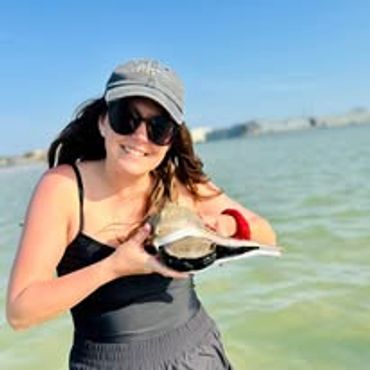 Woman smiling while holding a small turtle by the water.