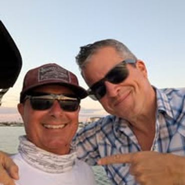 Two men wearing sunglasses smiling outdoors at sunset.