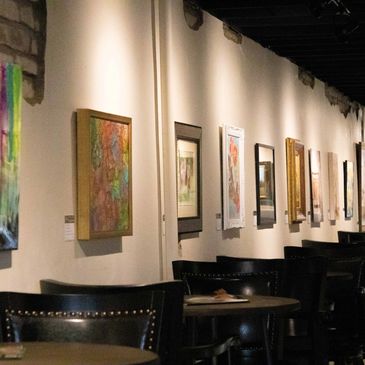 Art gallery with paintings on white walls and seating area.