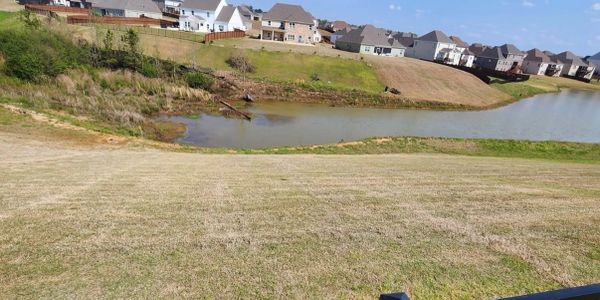 A suburban neighborhood with a grassy hill and small pond under a clear blue sky.