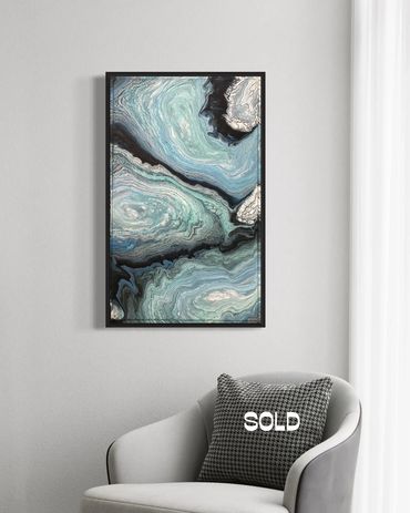 Abstract blue and black marbled painting above a modern chair with a 'SOLD' pillow.
