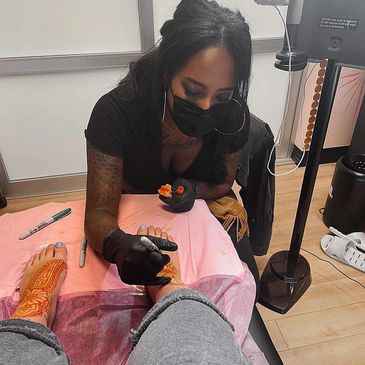 Tattoo artist working on intricate foot henna designs in a studio.