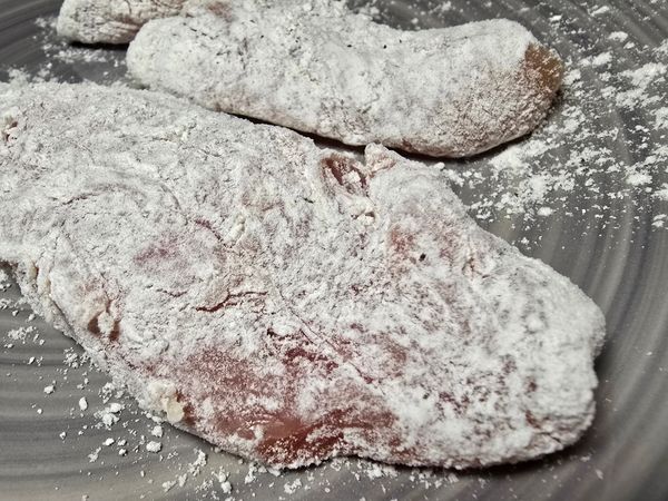 Raw meat pieces coated in flour on a plate.