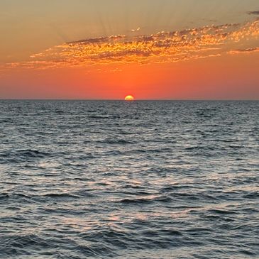 Sunset over a calm ocean with vibrant orange sky.