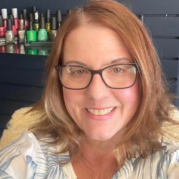 Smiling woman with glasses and nail polish bottles in the background.