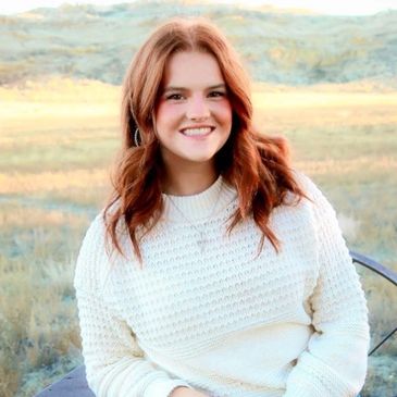 Young woman with red hair smiles outdoors in a white sweater.