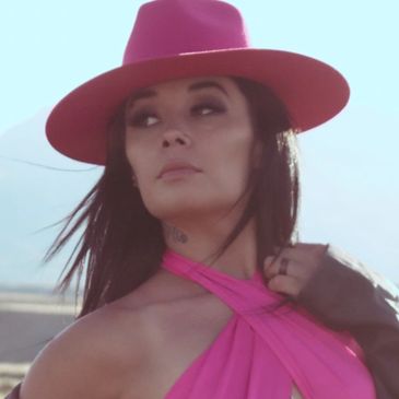 Woman in a bright pink hat and matching halter top looking away.