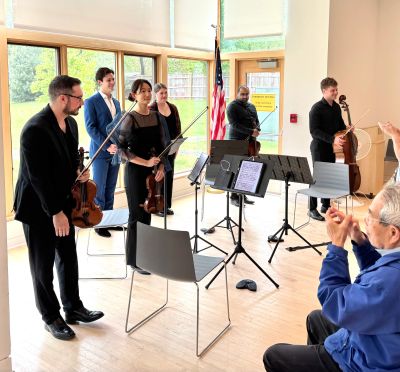A string quintet receives applause after a performance in a bright room.