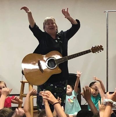Woman playing guitar with children raising their hands.