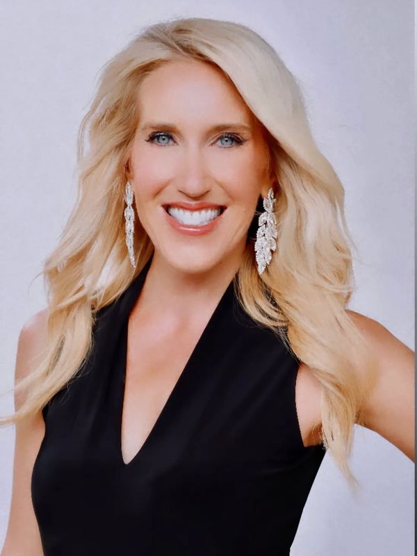 Smiling blonde woman in black dress with long earrings.