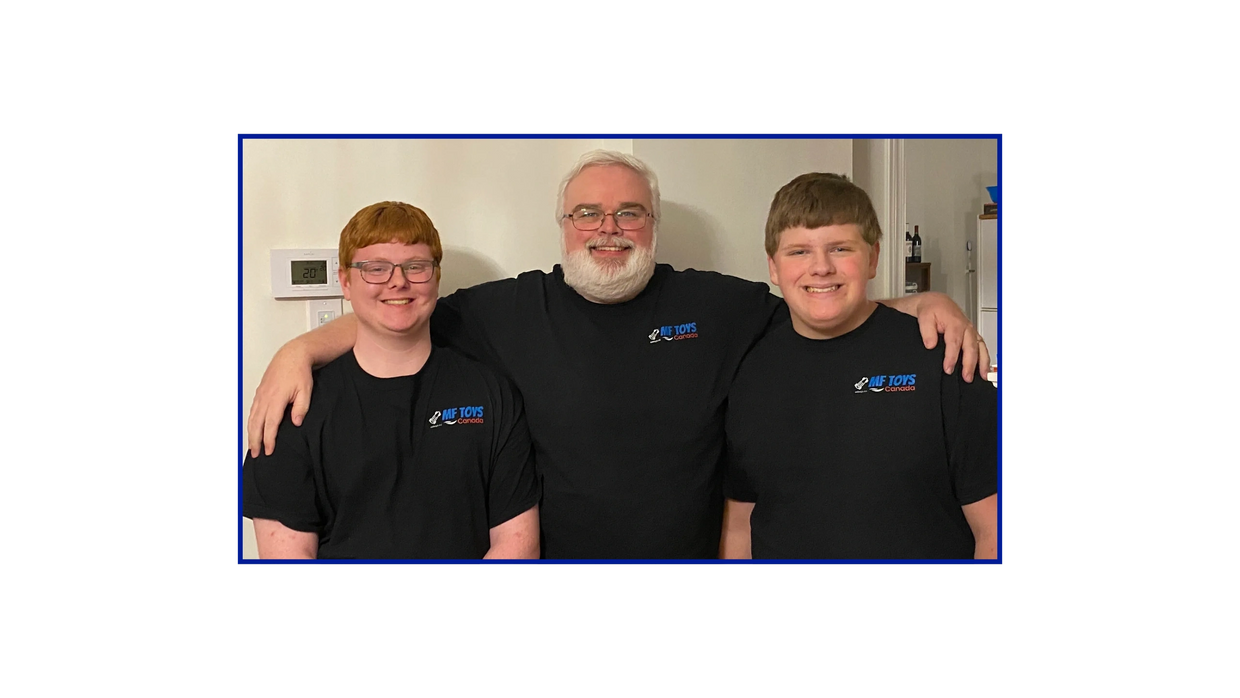 Three smiling men wearing matching black MF Toys Canada t-shirts pose together indoors.