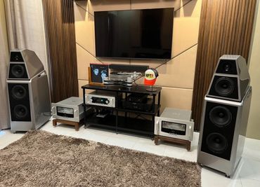 High-end home audio setup with large speakers, amplifiers, and a turntable under a wall-mounted TV.