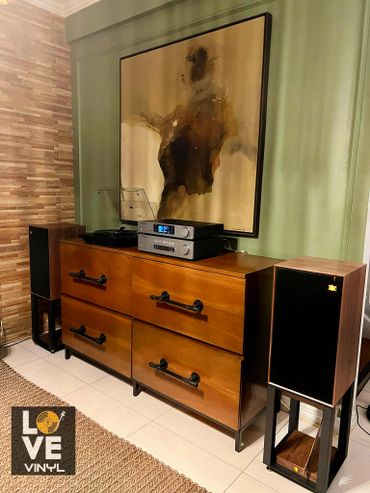 Vintage stereo setup with speakers and abstract art above a wooden cabinet.