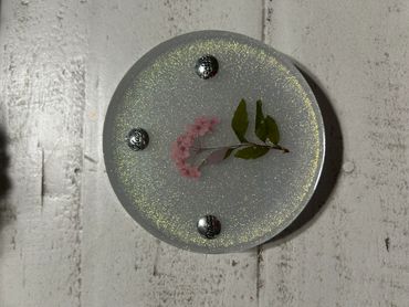 Round resin coaster with embedded pink flower and inspirational words.