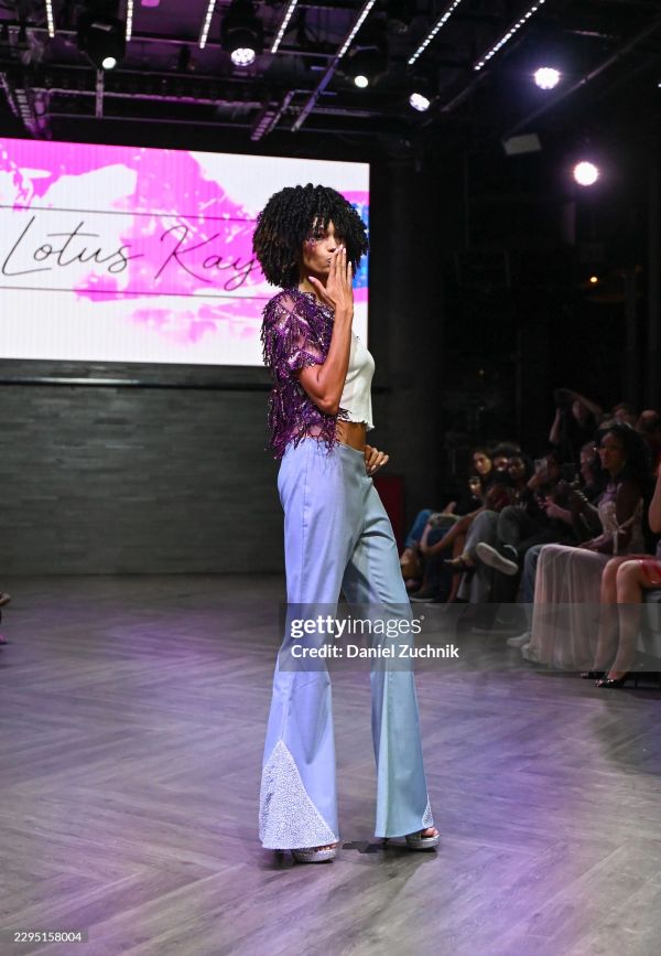 Model blowing a kiss on runway at fashion show.