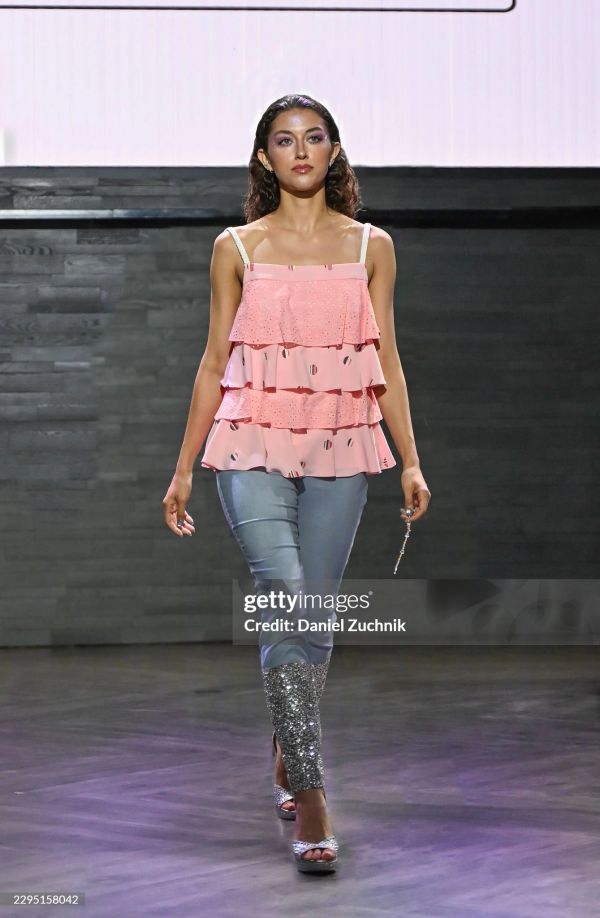 Model walking on runway in pink ruffle top and glittery pants.