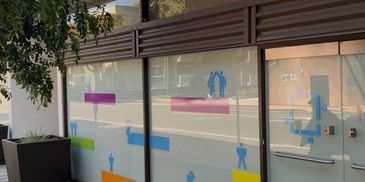 Frosted glass storefront with colorful geometric shapes and silhouettes.