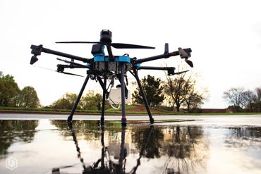 A large drone with multiple rotors standing on wet ground outdoors.