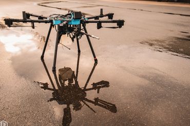 A drone with multiple arms reflected in a puddle on the ground.