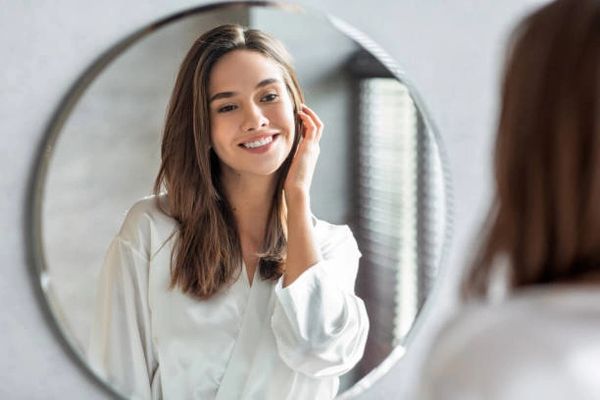 A woman smiles at her reflection in a round mirror.