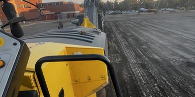View from a yellow construction vehicle operating on a dirt lot at sunset.