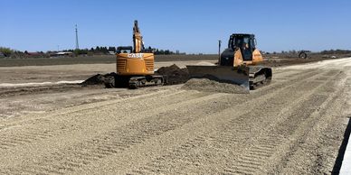 Construction vehicles leveling dirt under a clear blue sky.