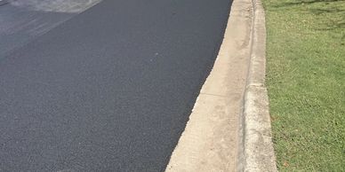 Steamroller paving a fresh layer of asphalt on a road under sunny conditions.