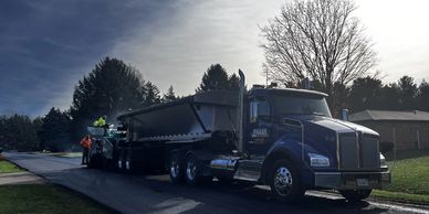 Truck and workers paving a road on a sunny day.